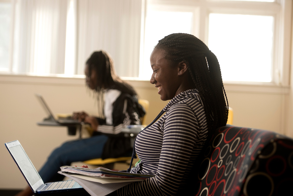 Two students study and smile in front of their laptops. 