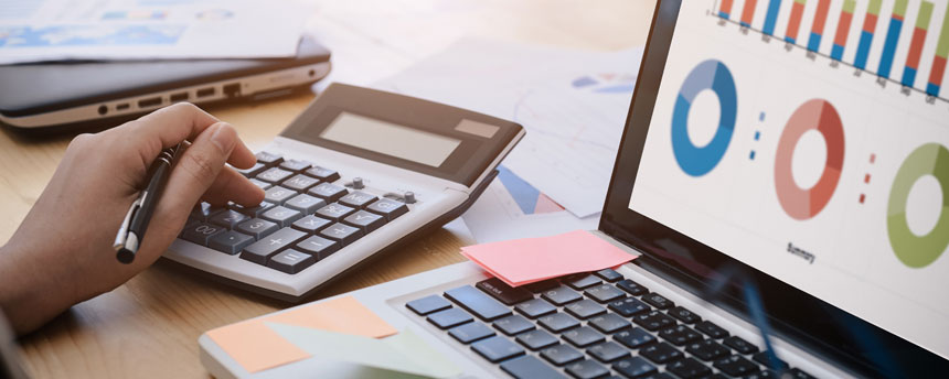 hand holding pen above desk calculator and laptop