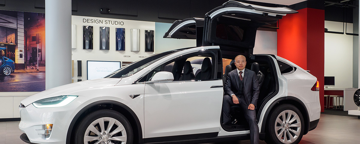 Business school alumnus James Chen posing with a Tesla