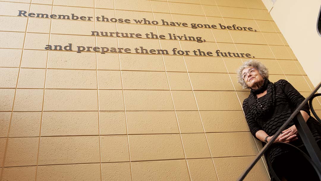 Woman stands in front of sign that reads: Remember those who have gone before...