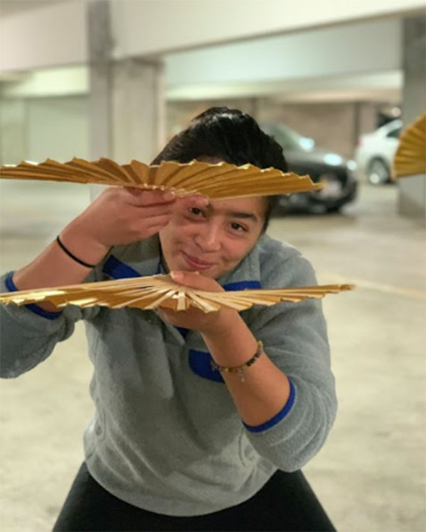 Kimiko Masaki, a third-year biochemistry and molecular biology major, peeks through a fan during MK Vintage rehearsal.