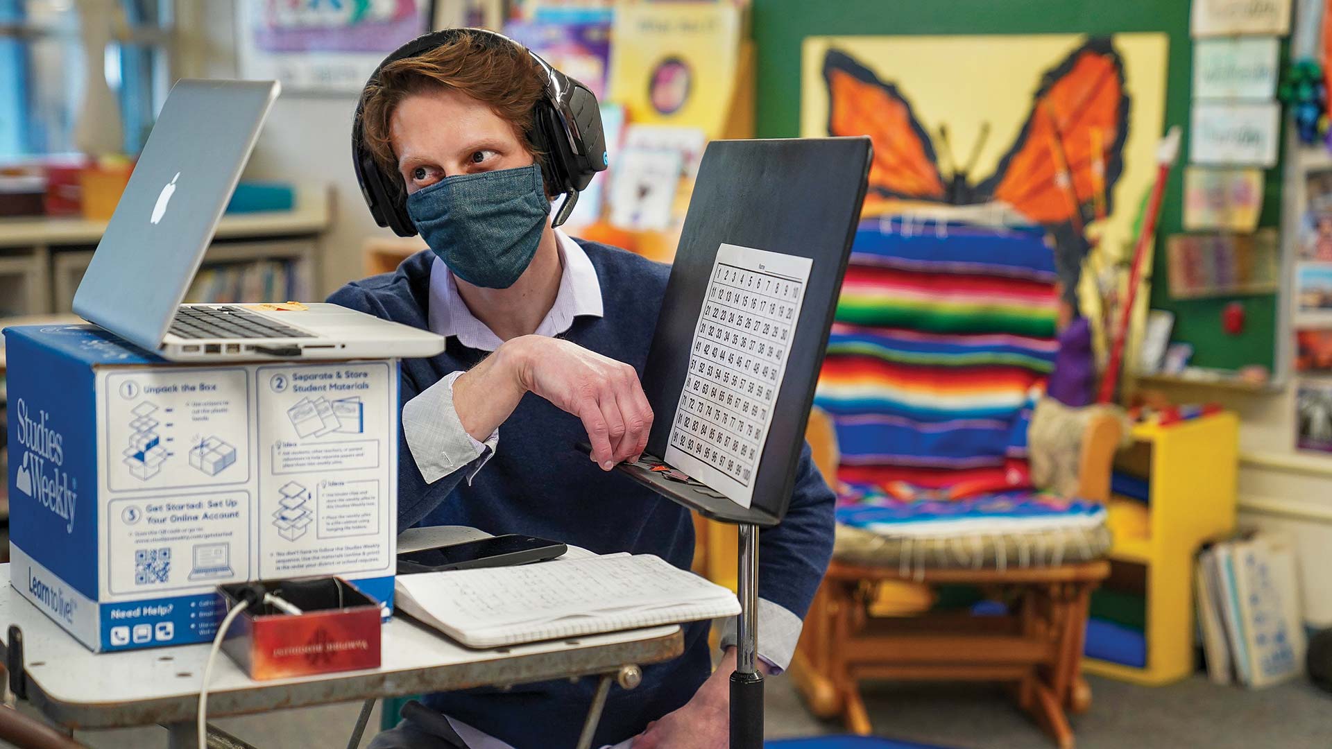 a man wears a mask and looks ino a computer while teaching