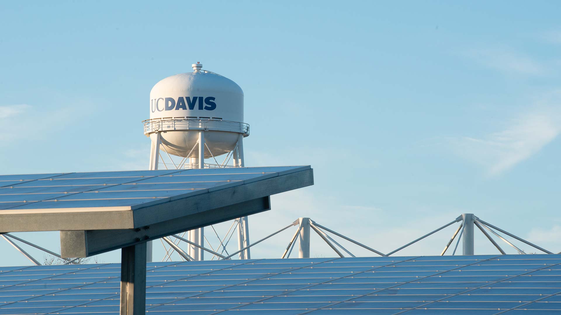 A UC Davis water tower peeks above a set of solar panels.