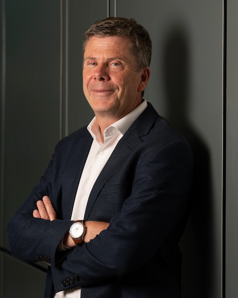 Portrait photograph of a smiling Simon Cherry in navy blazer, arms crossed