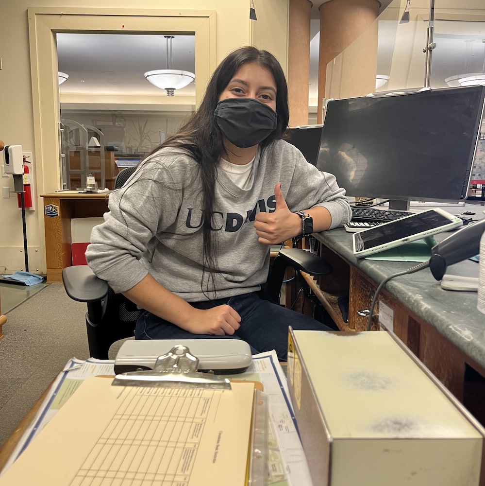 A student holds a thumbs up at her on-campus job at UC Davis. 