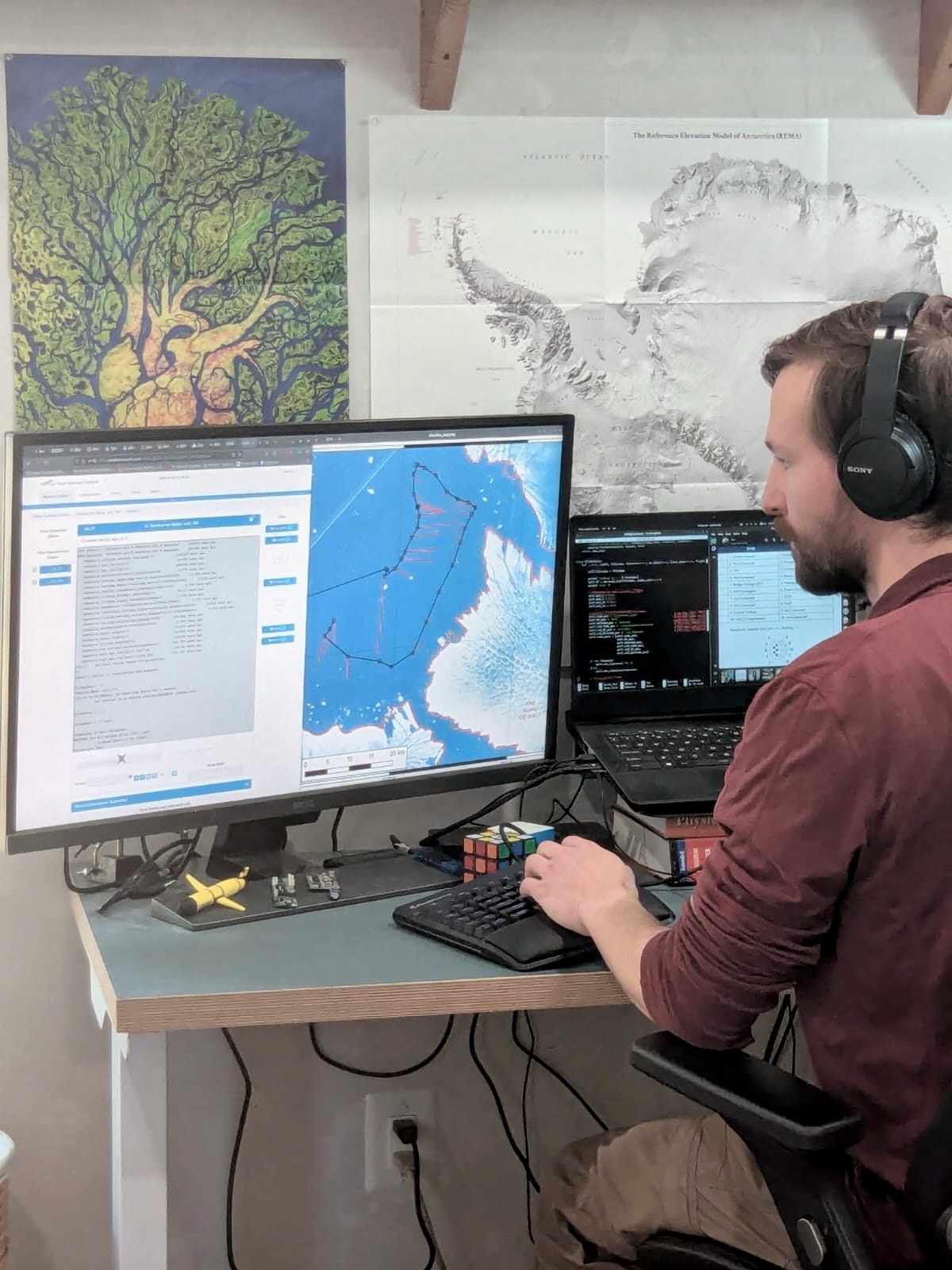 Kenneth Larriue sits at desk in front of computer screen with map of Antarctica