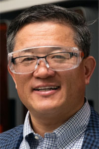 Smiling man in clear safety goggles and checked shirt, close-up headshot