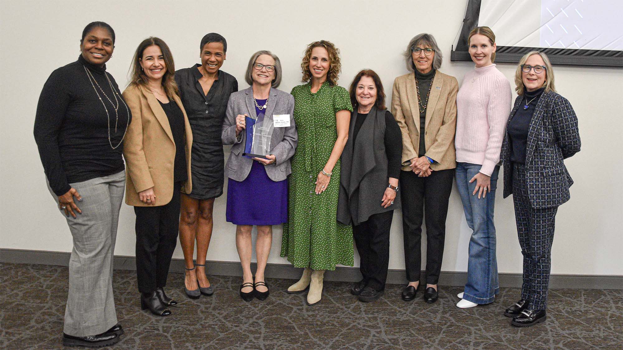 Group of eight women pose for photo with Amy Brooks-Kayal, who is holding an award.