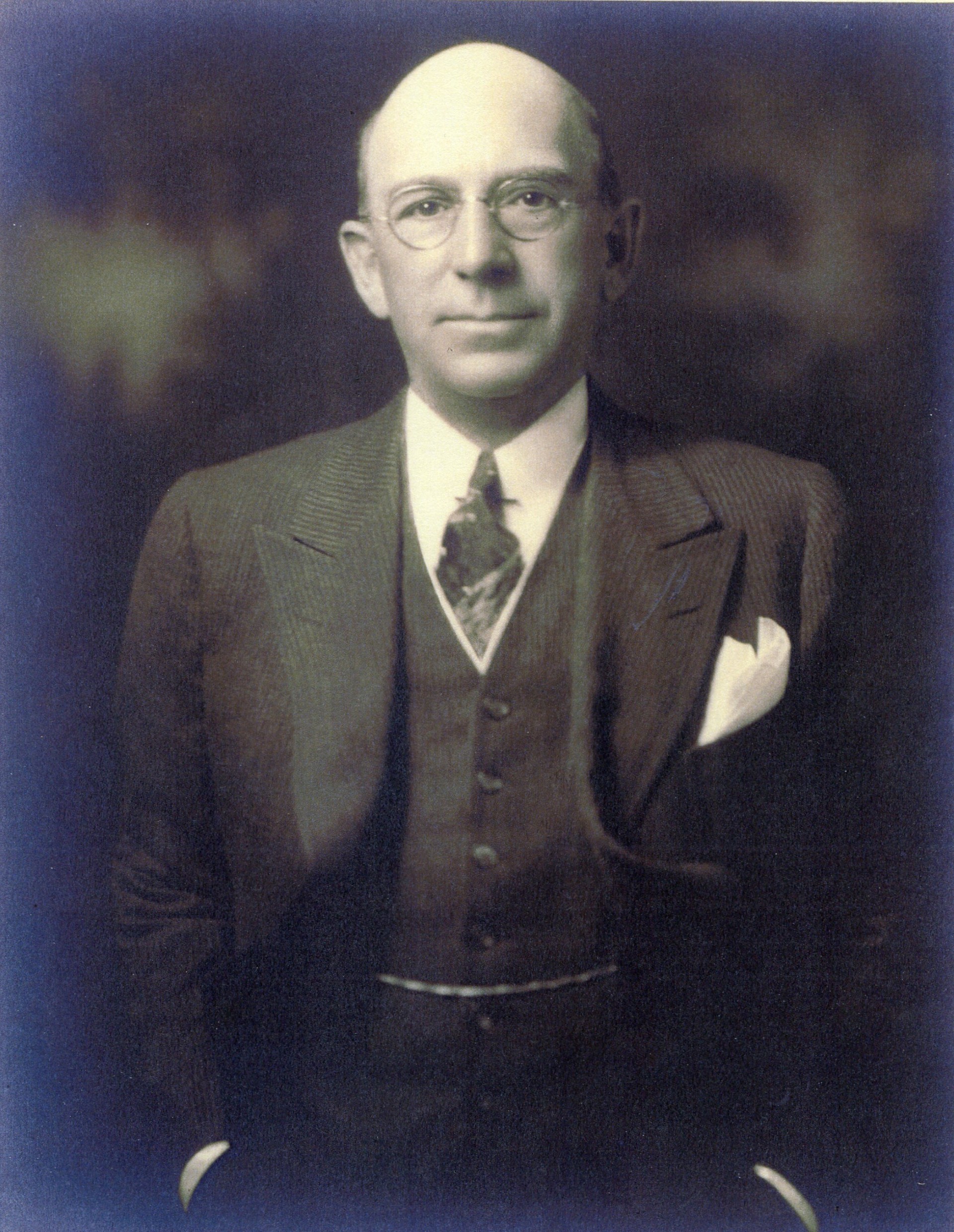 A well-dressed man in a dark suit stands confidently, hands in pockets, smiling. Portrait C.L. Best, 1878-1951 (Courtesy) 