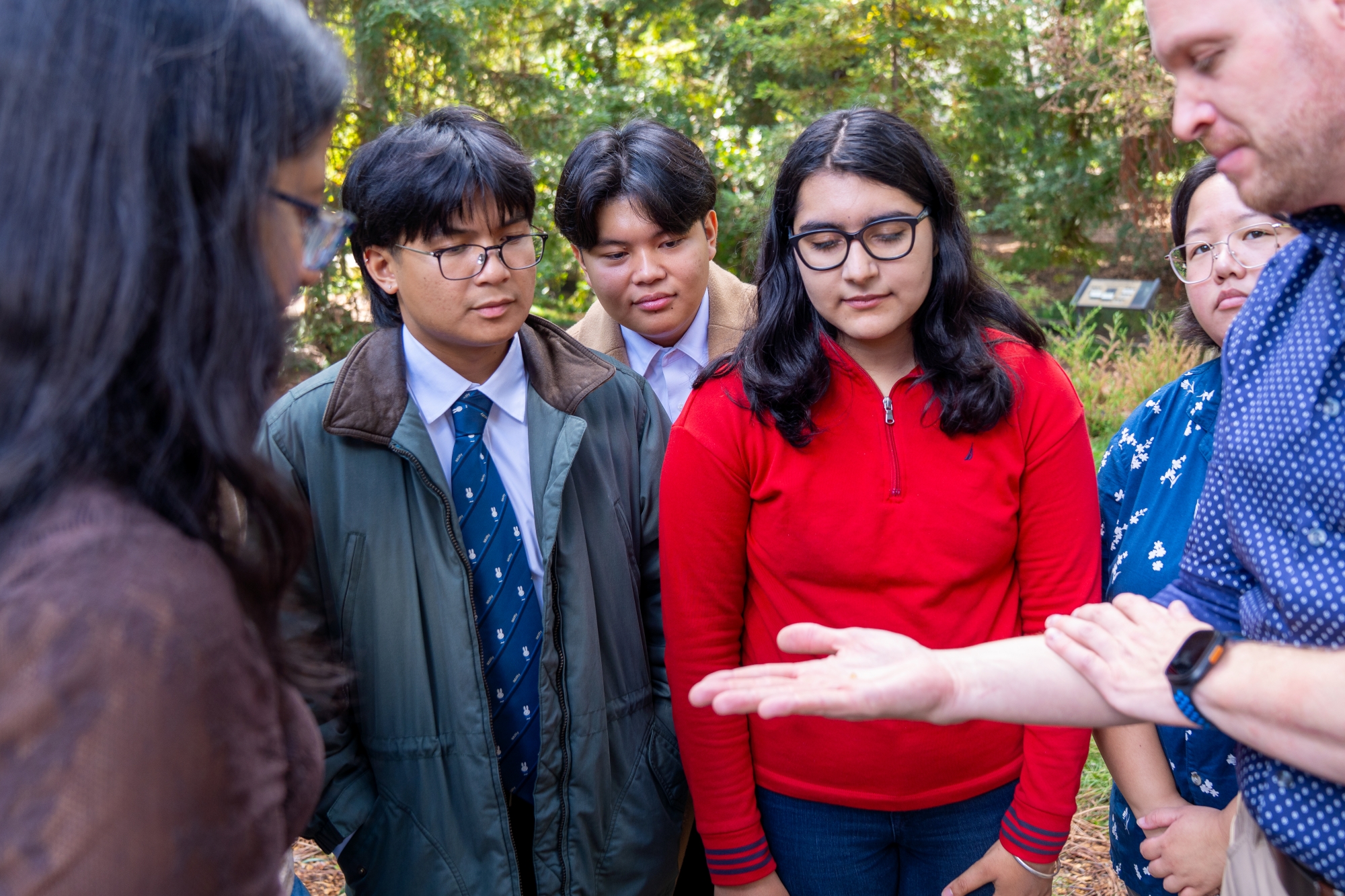 Diverse group of teens outdoors watching a man show his palms