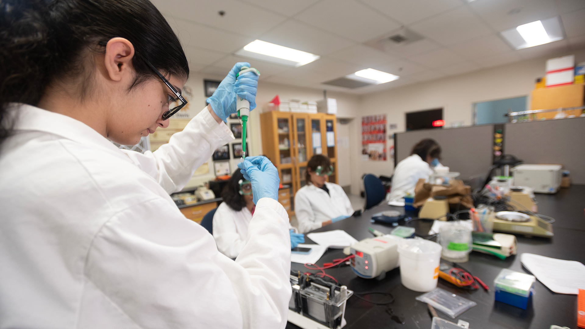 Student stands in a lab with a pipette in her hands