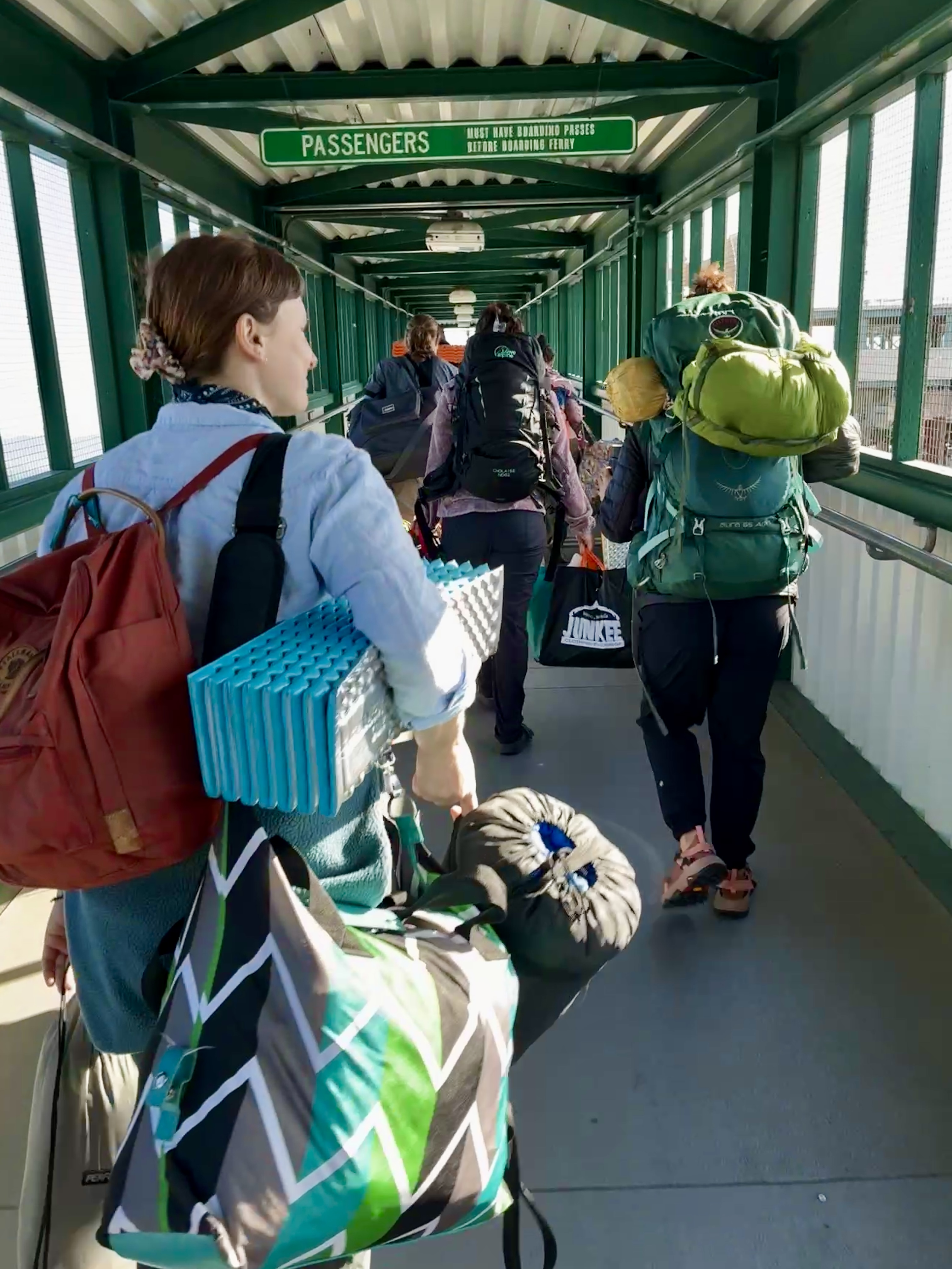 Passengers walking through covered green walkway carrying backpacks and luggage