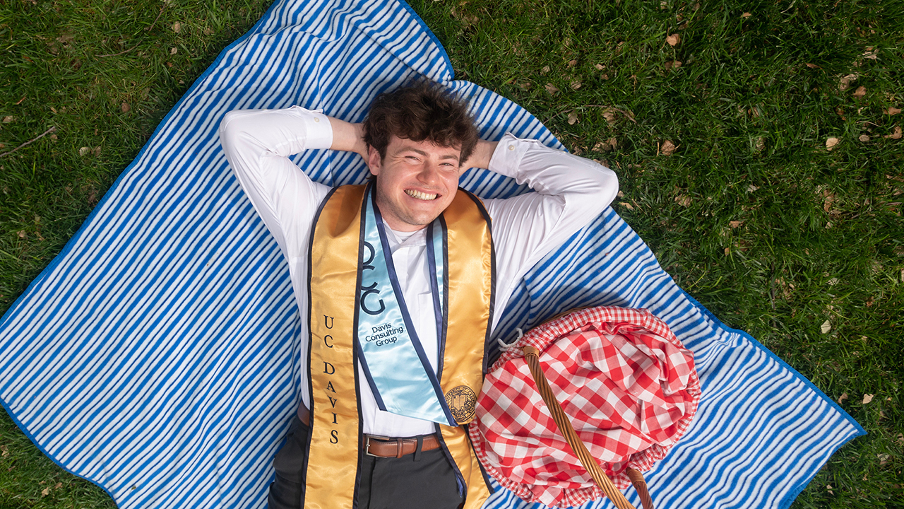 Shot from above, Jesse Goodman lies on a blue picnic blanket beside a picnic basket.