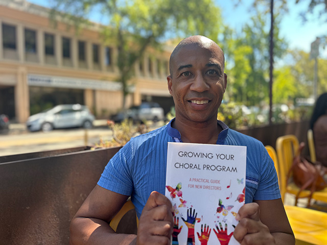 man holding book with building behind him