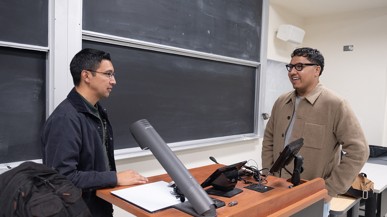 Emmanuel Pereida Garcia and his instructor talk in front of a classroom blackboard