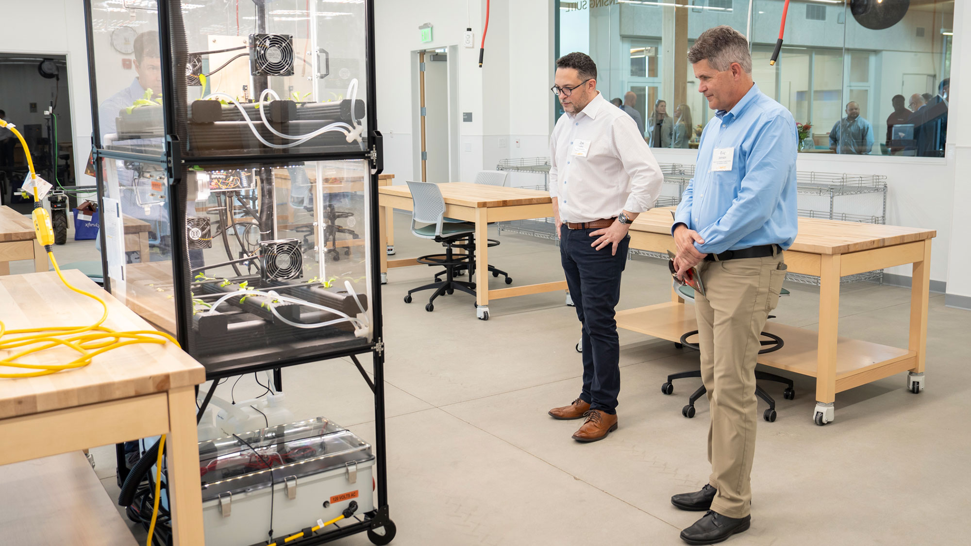 Two people in collared shirts examining robotic equipment on a cart in a bright lab