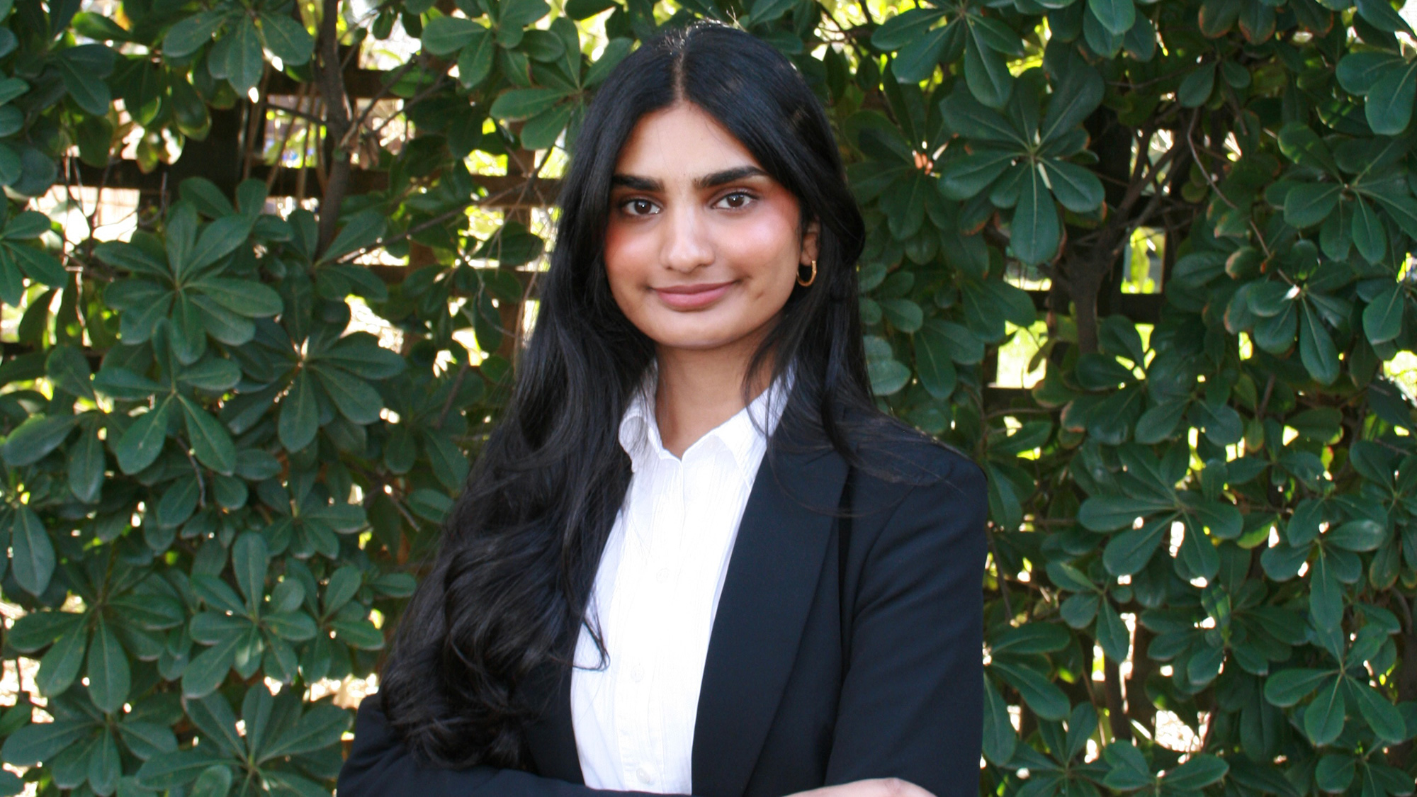 Outdoor professional headshot of a smiling woman with long dark hair, arms crossed