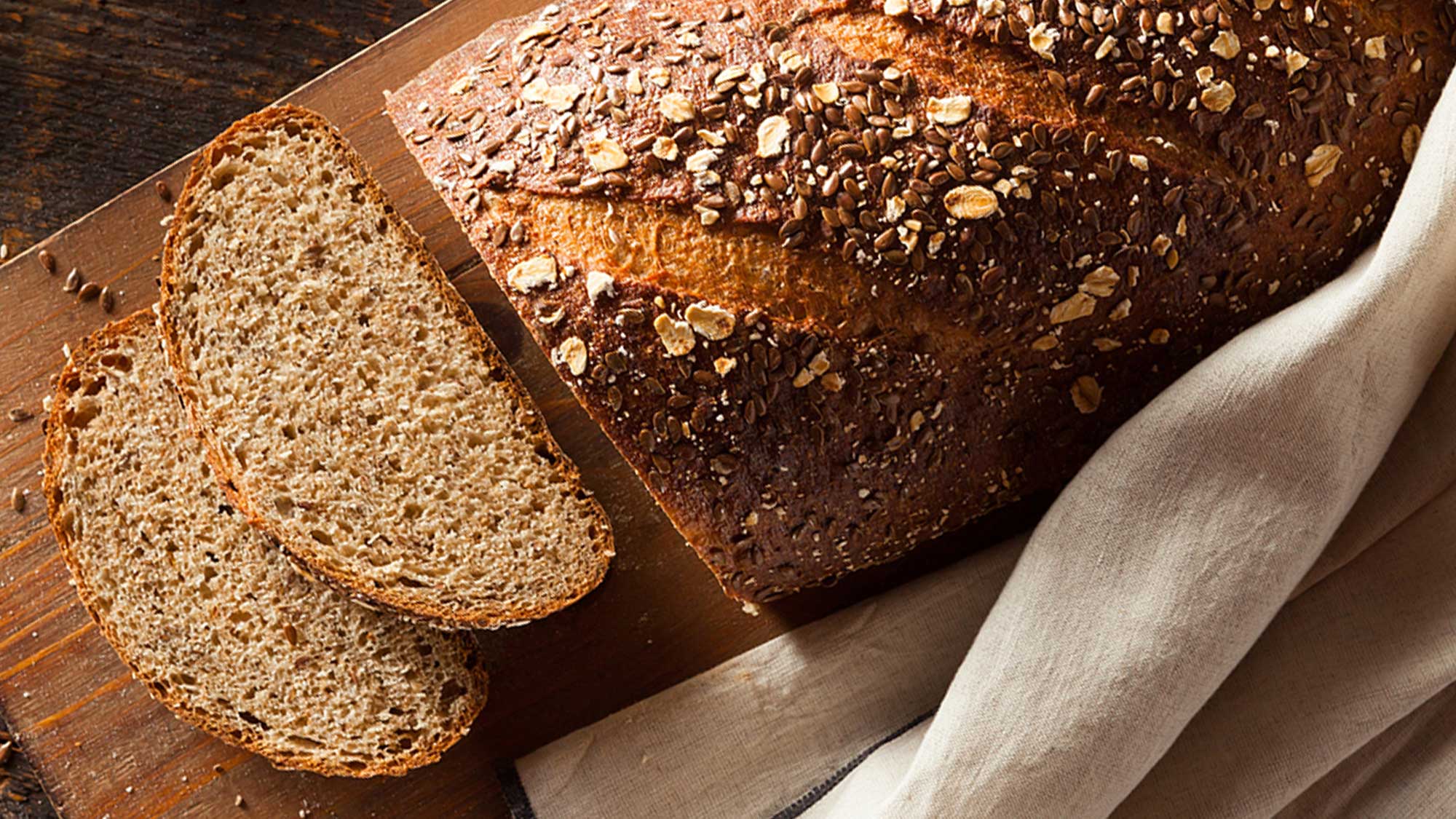 Photo of a loaf of whole grain bread on a cutting board. Two slices have been cut to reveal the inside of the loaf.