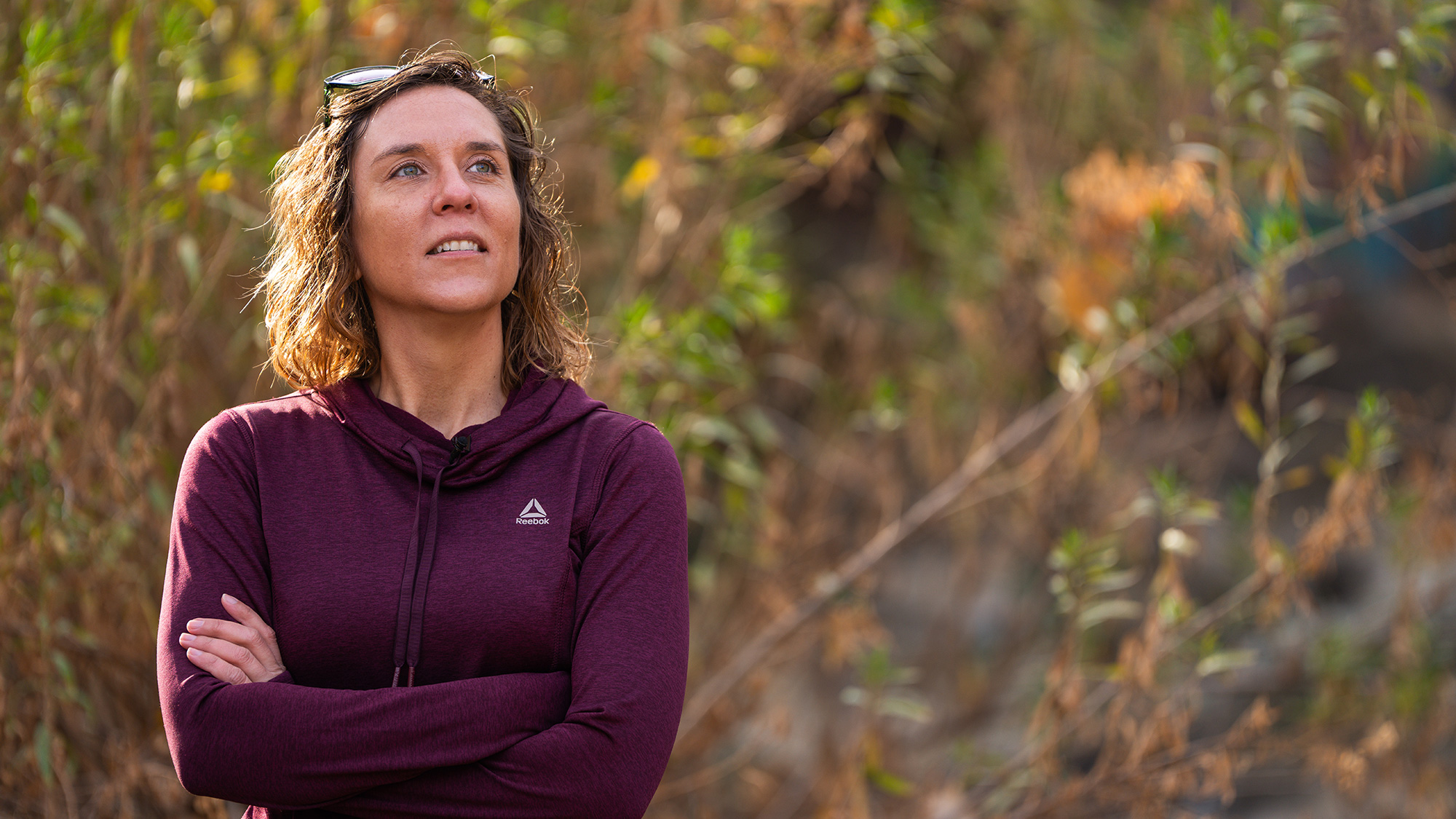 Woman stands outside with her arms crossed and looks up