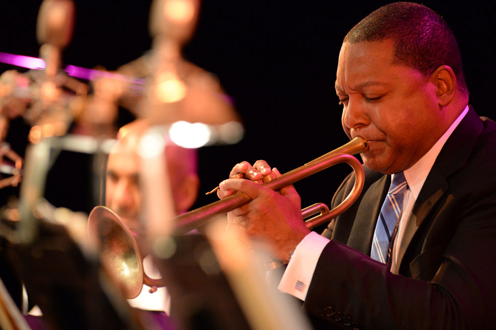 Trumpeter in suit playing on stage under warm, purple-tinged lighting