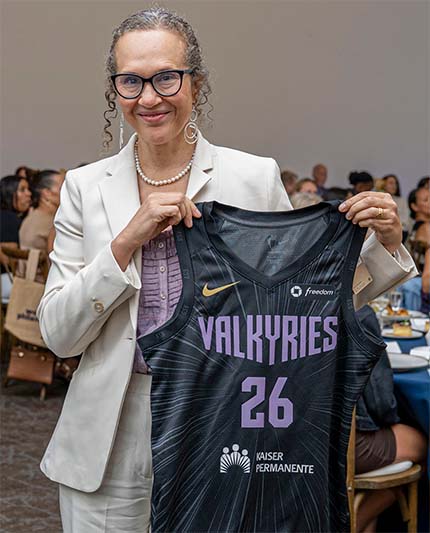 Smiling woman in white suit holding black Valkyries jersey number 26