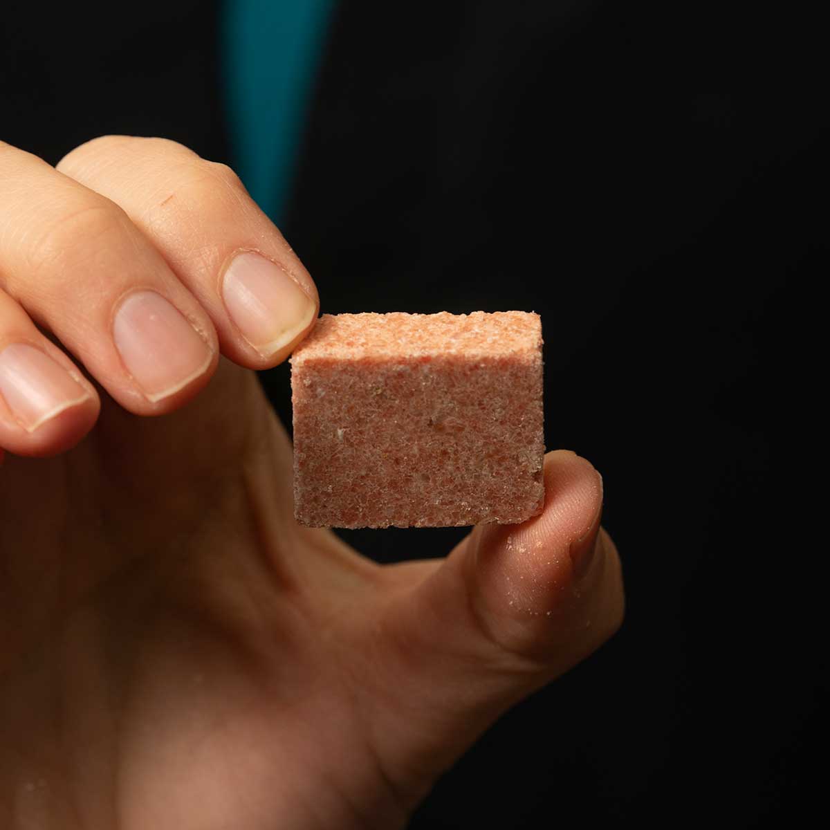 Closeup photo of a woman's hand holding a pinkish block between her thumb and index finger.