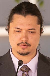 Portrait of a man in suit with tied-back hair speaking into a microphone