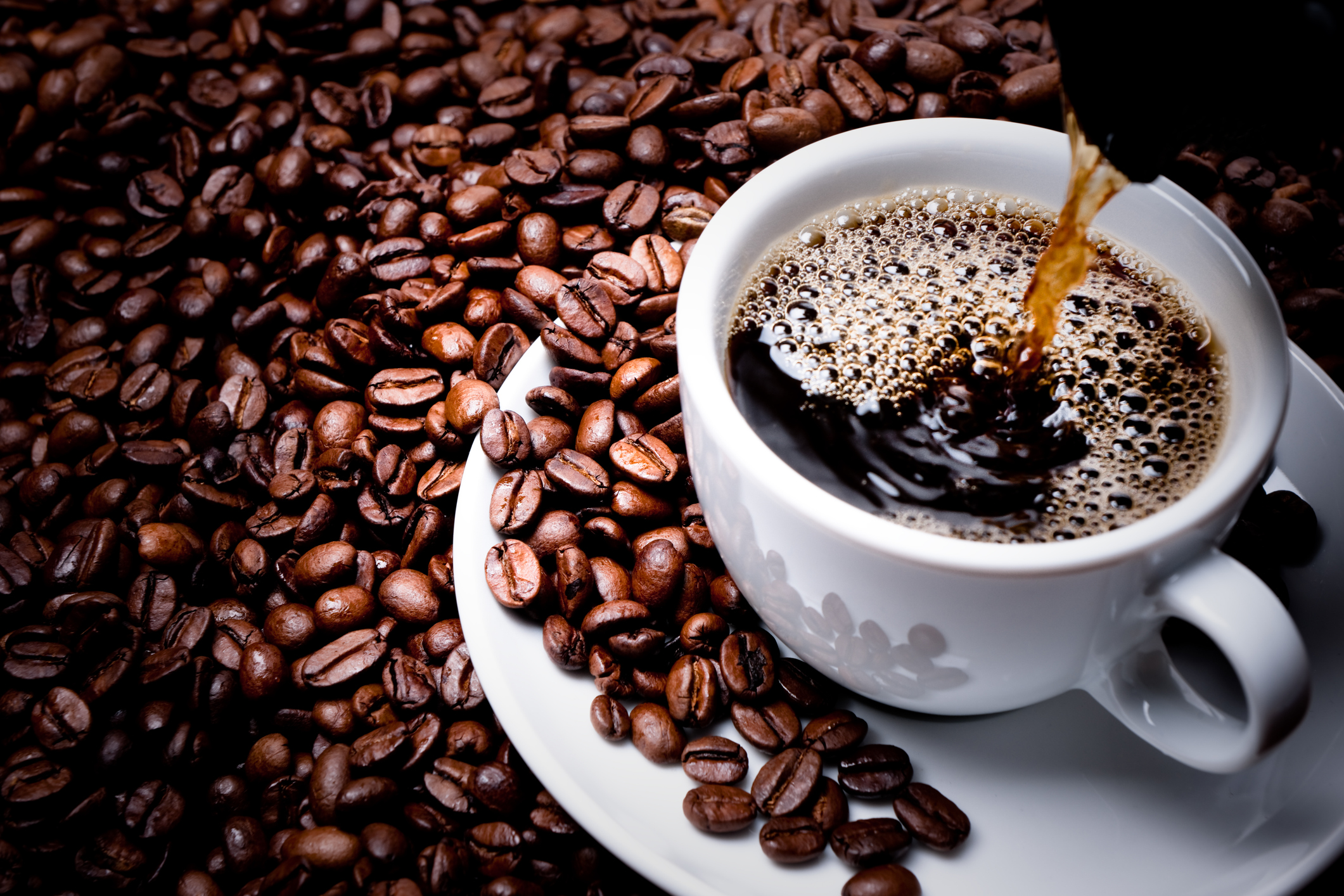 Coffee being poured into a cup surrounded by coffee beans