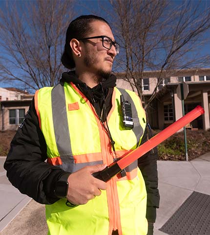 Man wearing reflective vest and holding orange baton prepares to direct traffic