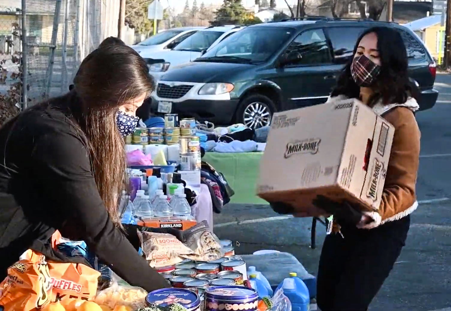 Woman lifts box onto table where another woman is arranging goods to be given away.