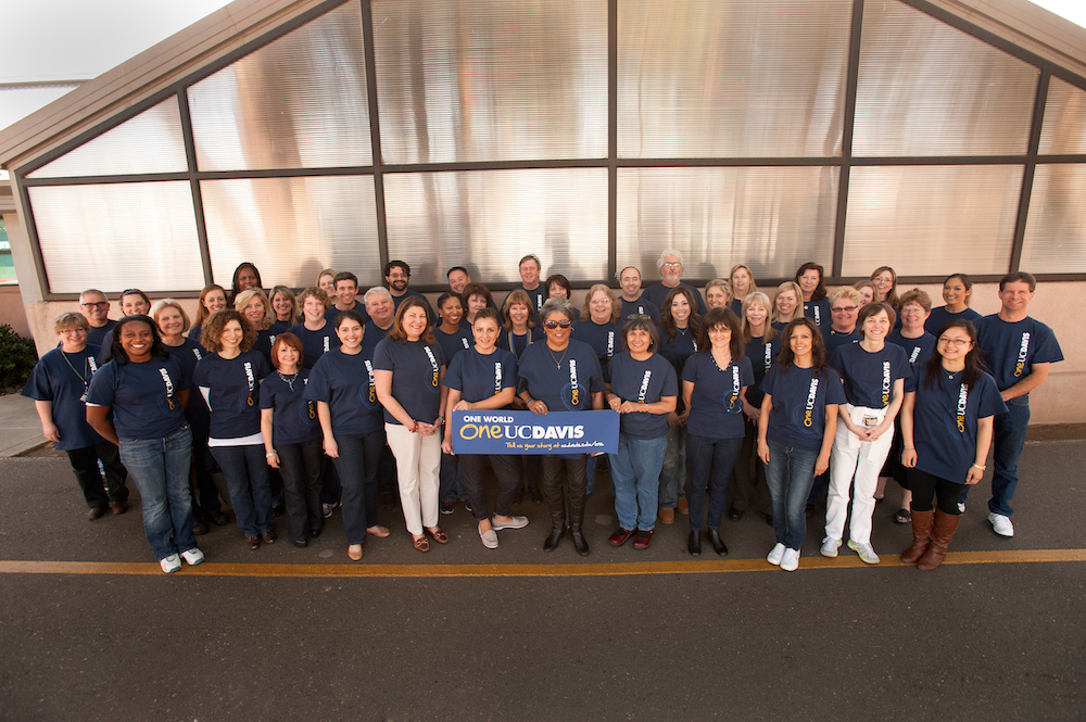 A crowd of human resources workers smiles together with a banner at UC Davis. 