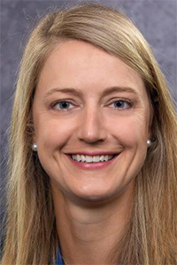 Smiling blonde woman headshot with pearl earrings and gray studio backdrop