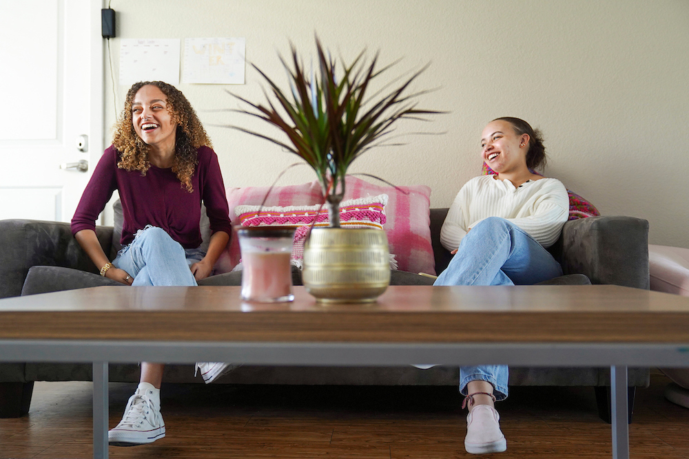 Two roommate laugh on their couch at UC Davis. 