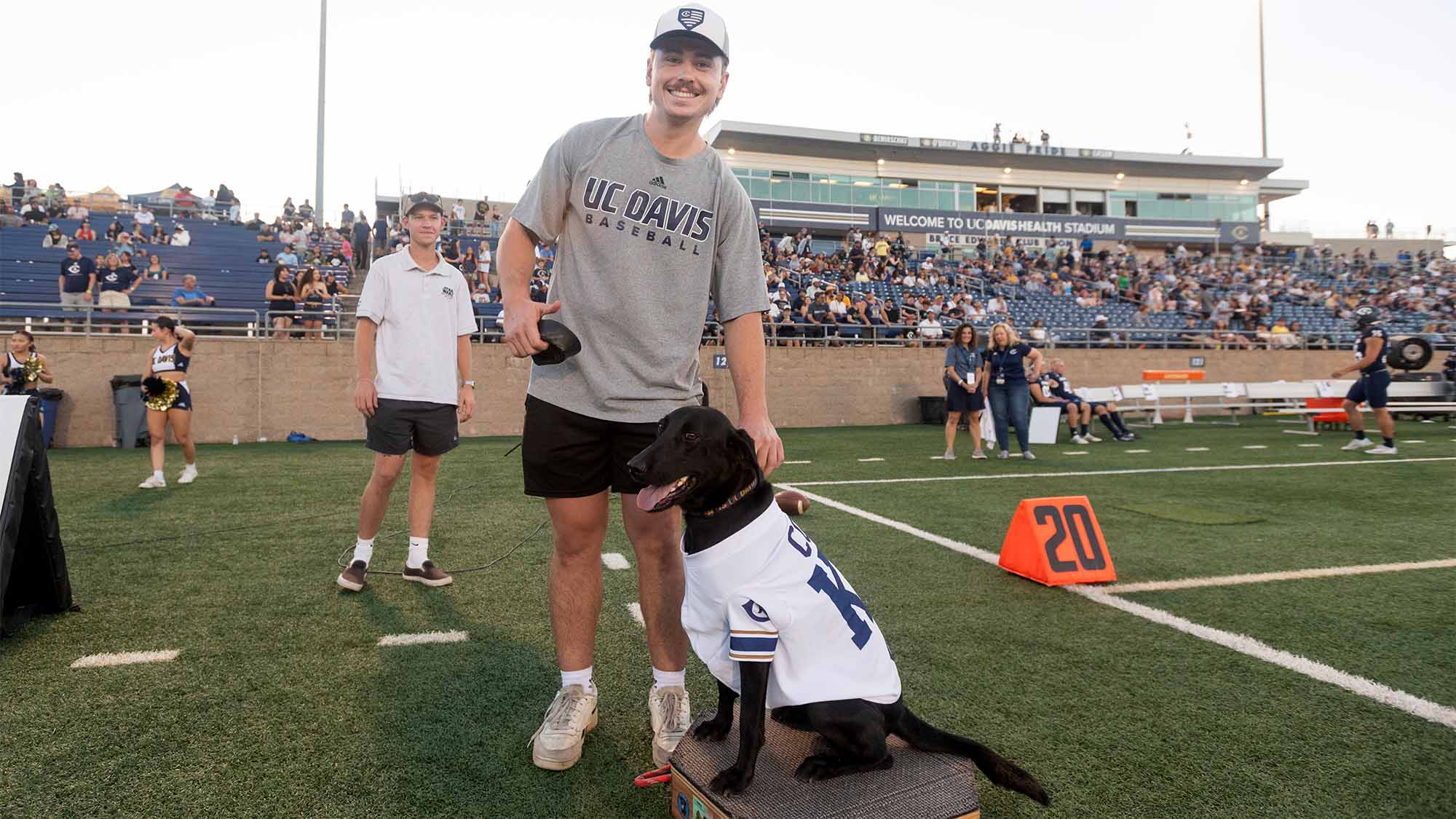 Student wearing UC Davis baseball t-shirt holds black labrador retriever