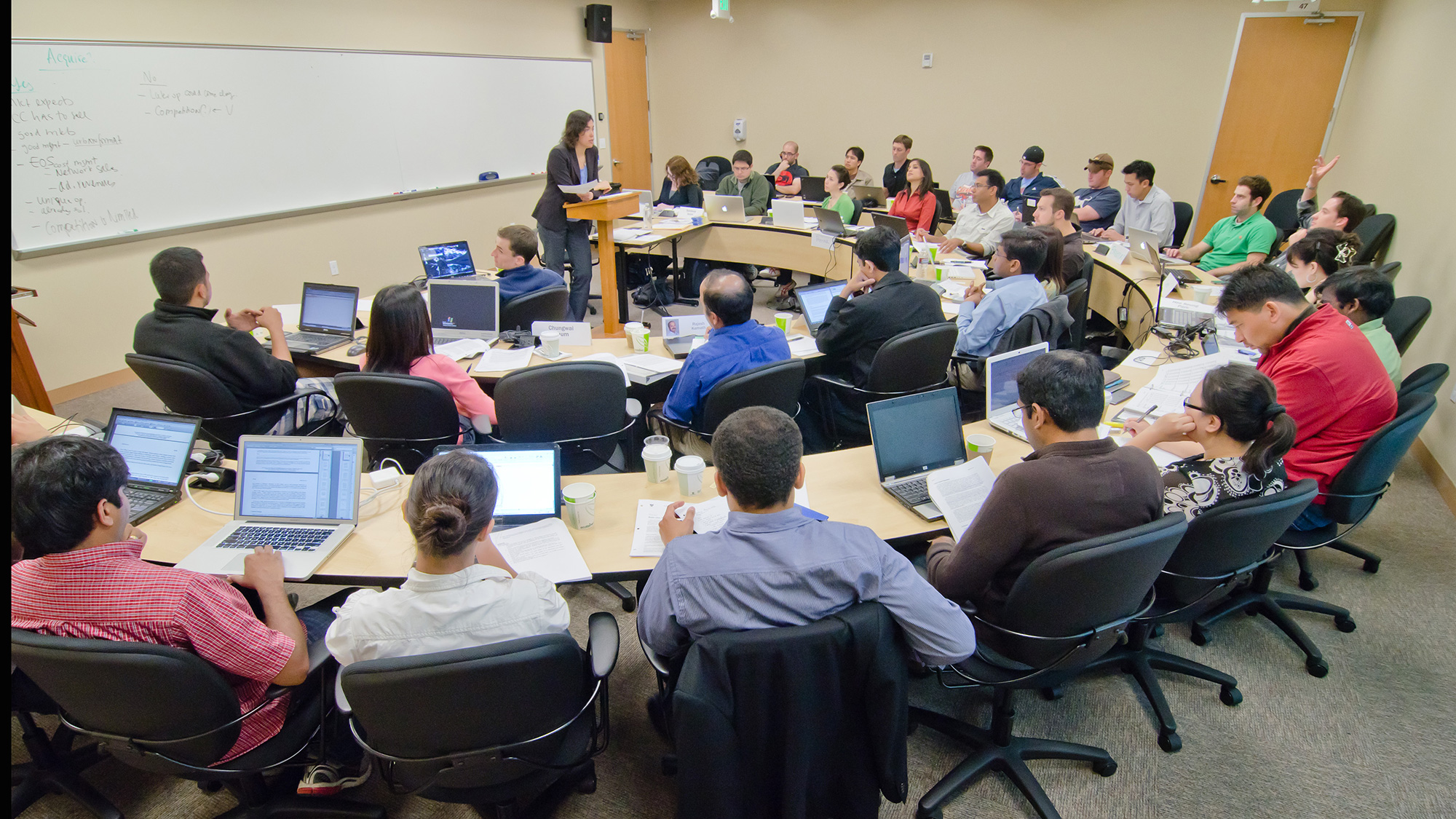 Students sit in semi-circle facing teacher in a classroom