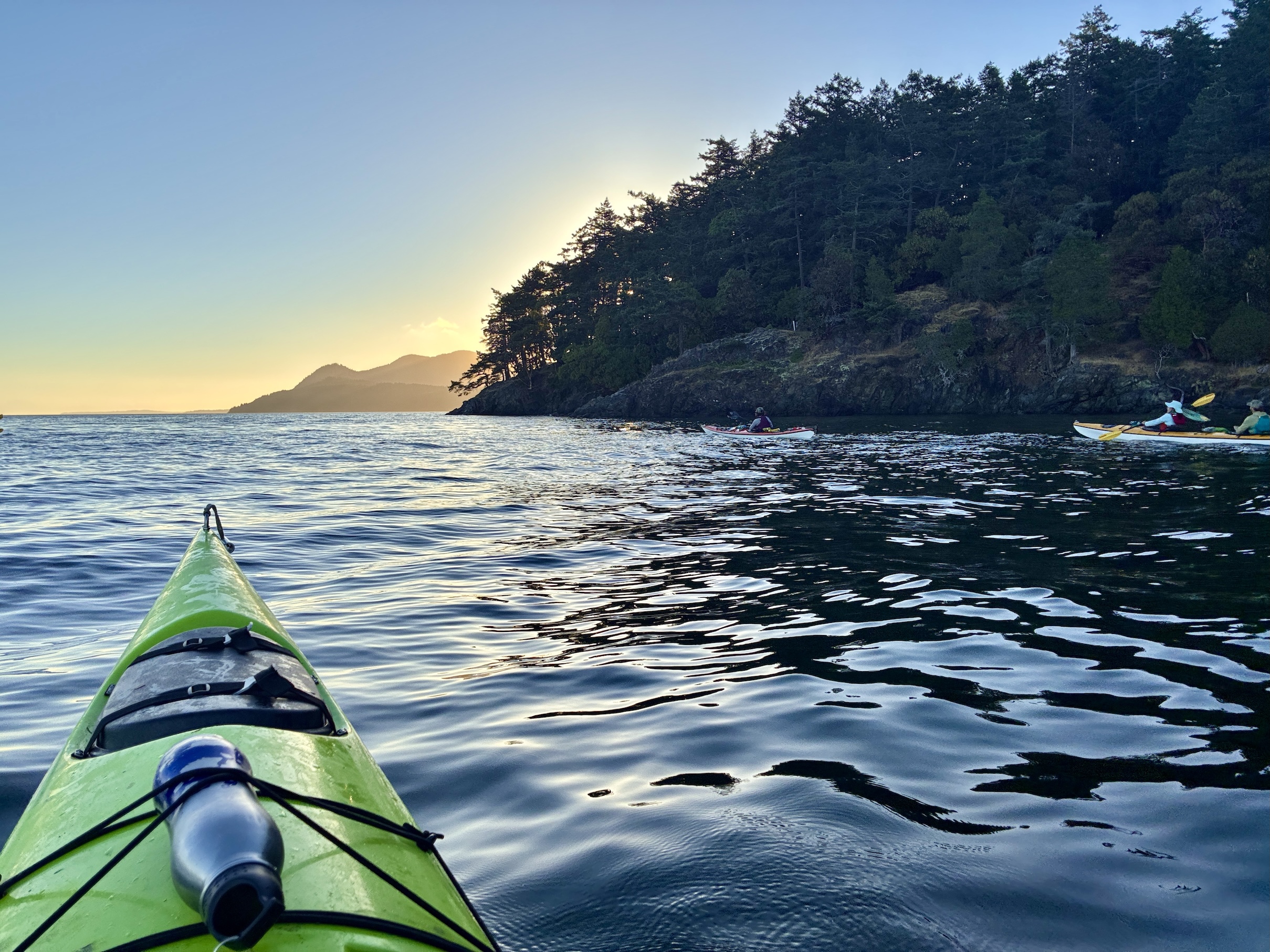 Serene green kayak bow on calm coastal water at sunrise with tree-covered headland