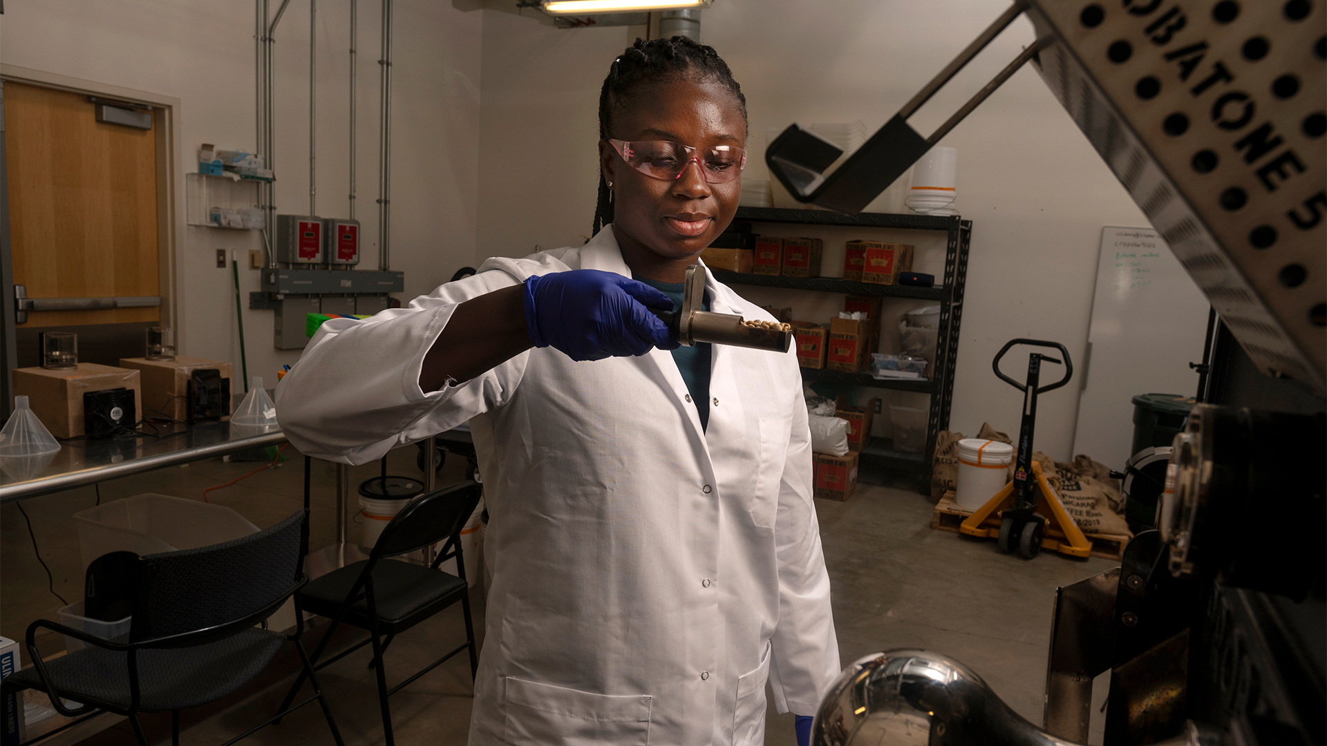 A woman wearing lab gear examines roasted coffee beans in a small tray.