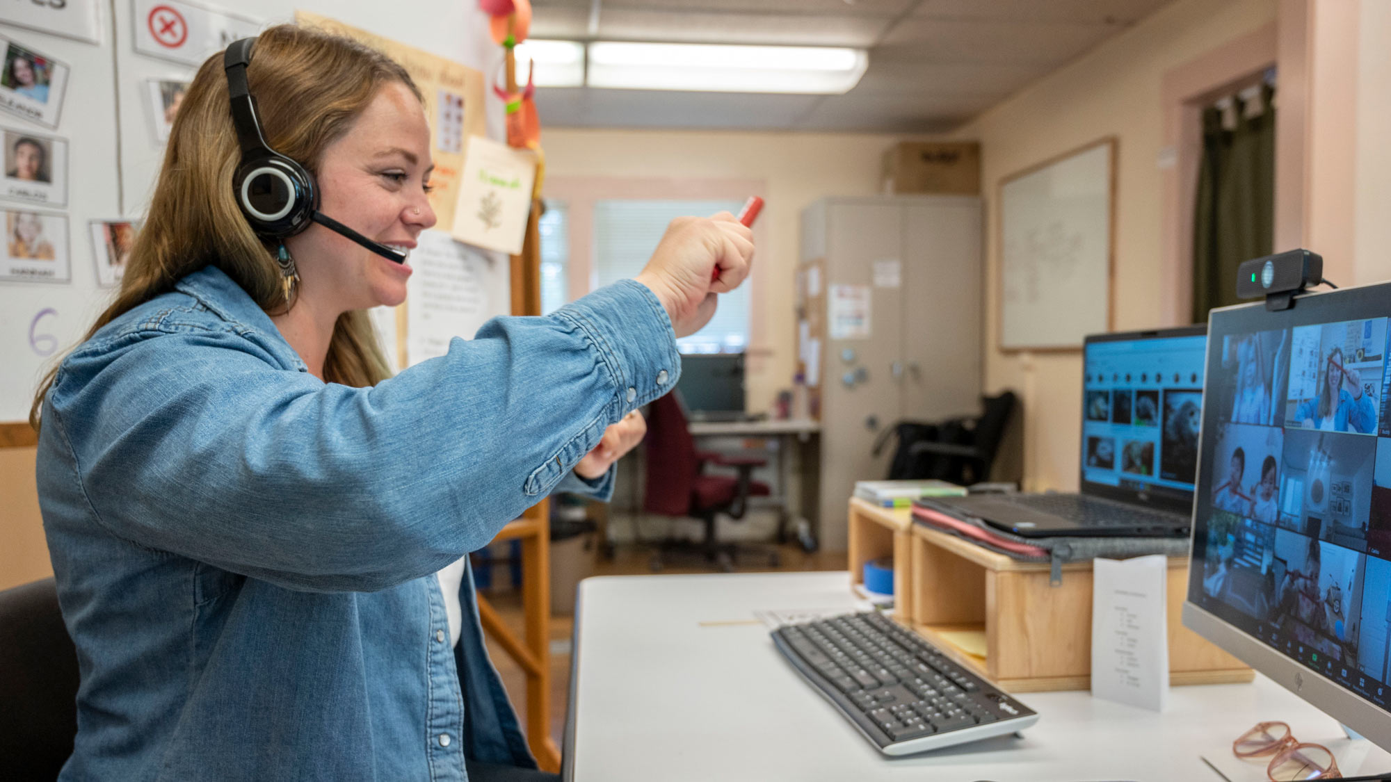 Teacher in front of computer monitor, addressing class on screen.