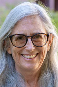 Smiling woman with long gray hair and tortoiseshell glasses, soft green background
