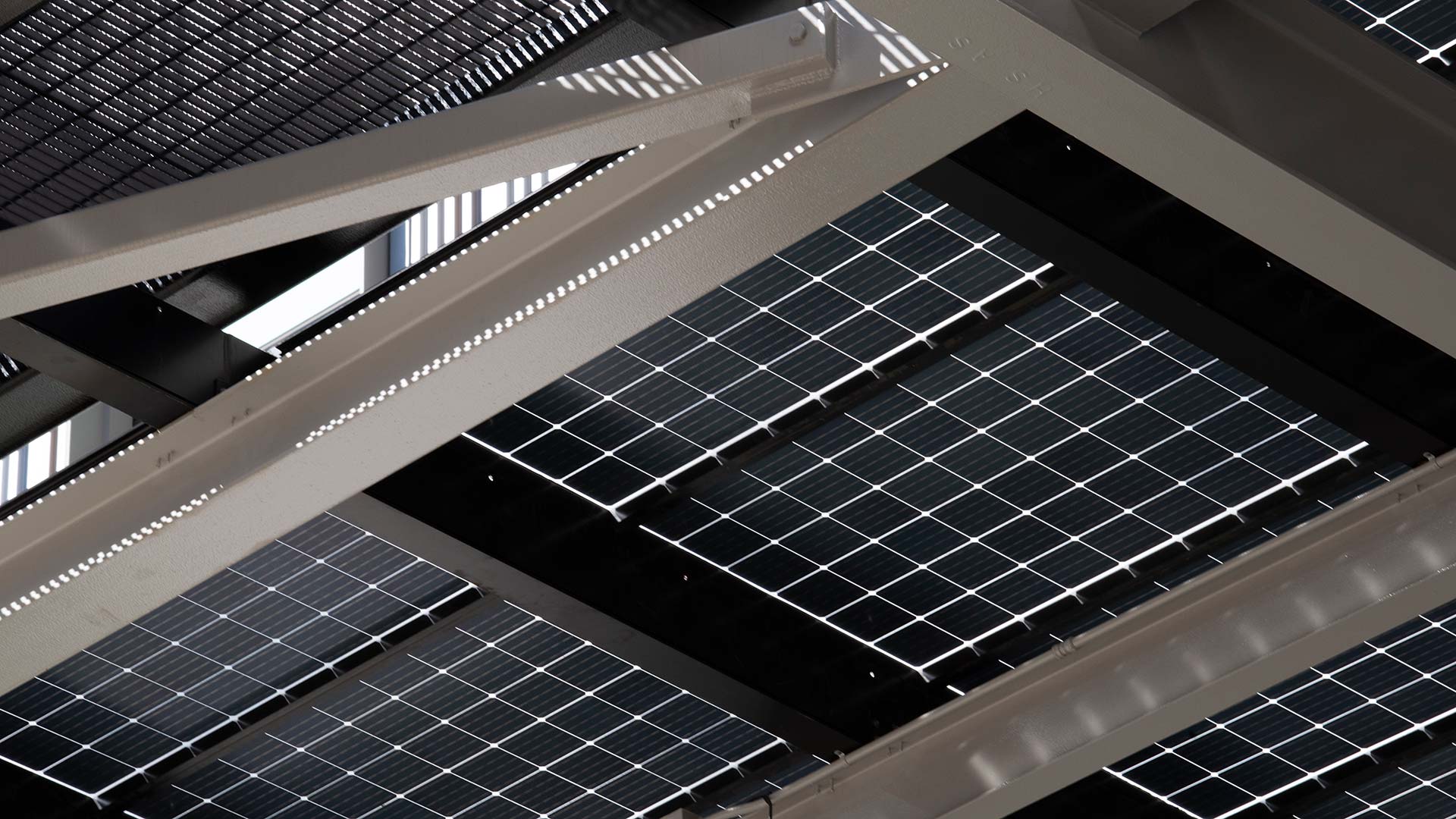 A view of solar panels from underneath. The panels form a shade structure for the outdoor space beside the building. The roof extends over the building and the outdoor space.