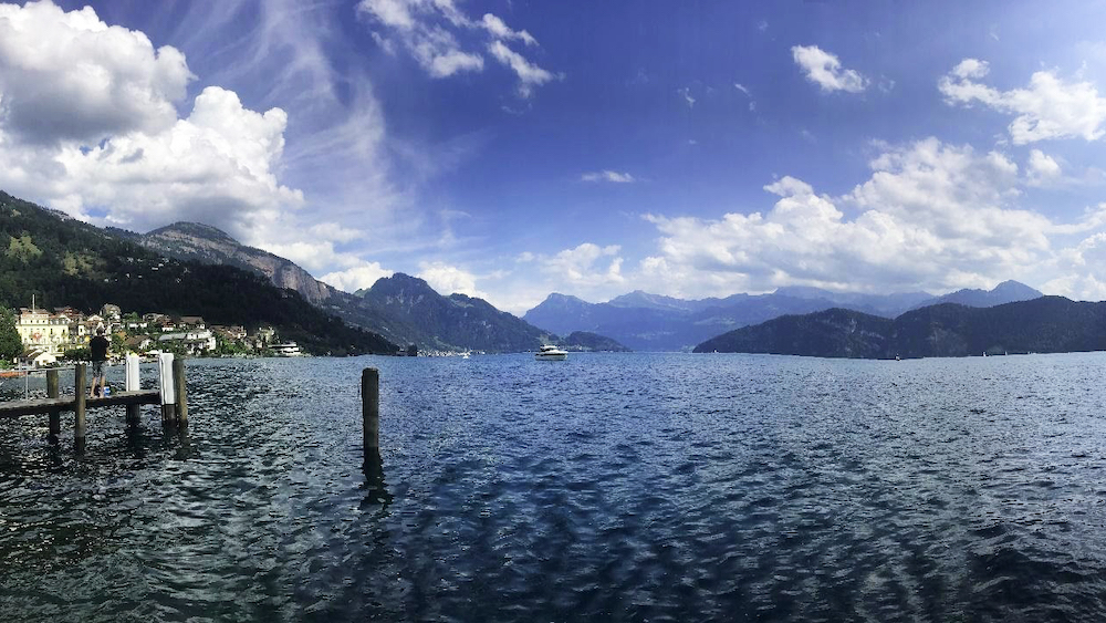 A sparkling lake surrounded by mountains and white fluffy clouds. 