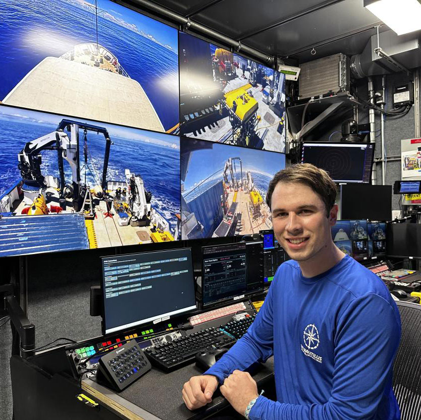 Smiling man at marine control console with multiple large underwater video screens