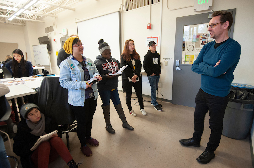 A professor stands in front of a class who are also standing up at UC Davis. 