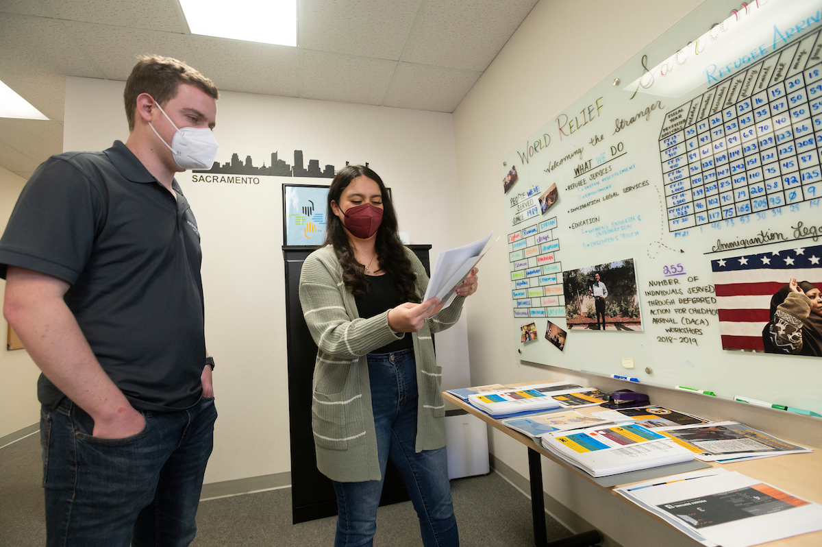 An intern talks with her supervisor in front of handouts and a whiteboard. 