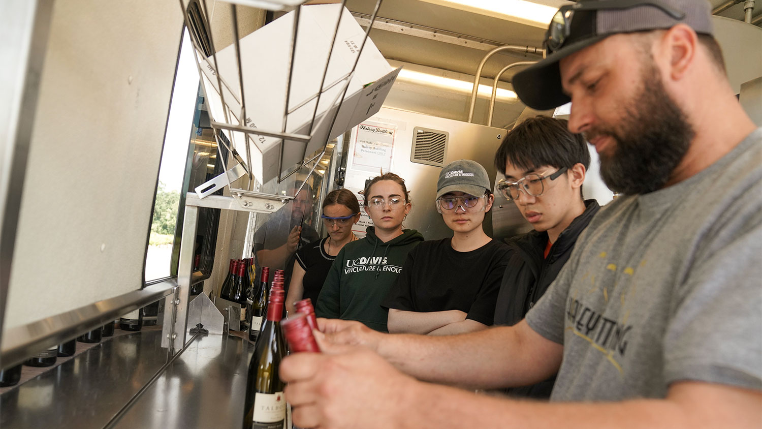 A Halsey Bottling employee demonstrates to VEN127L (post-fermentation processing) students how to remove bottled wine from the conveyor belt and package them in boxes. (Karin Higgins/UC Davis)