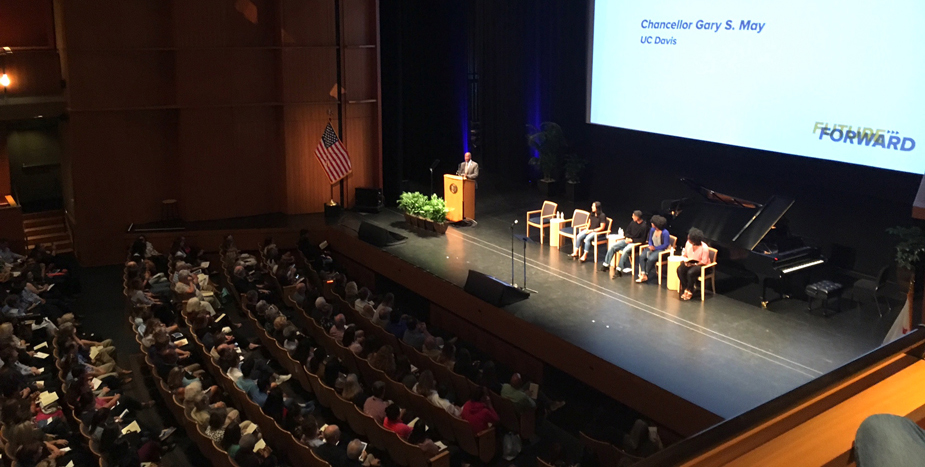 Chancellor at podium, wide shot showing stage party