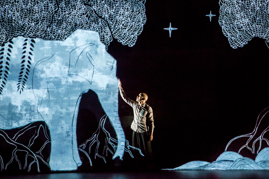 Scene from Akram Khan dance company’s “Chotto Dash,” showing a man touching an animated elephant.