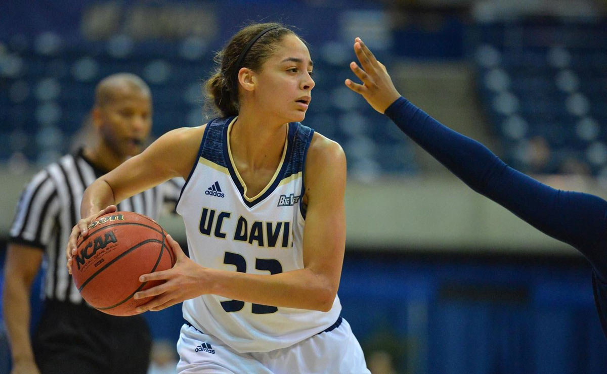 Basketball players keeps ball away from defender's outstretched arm.