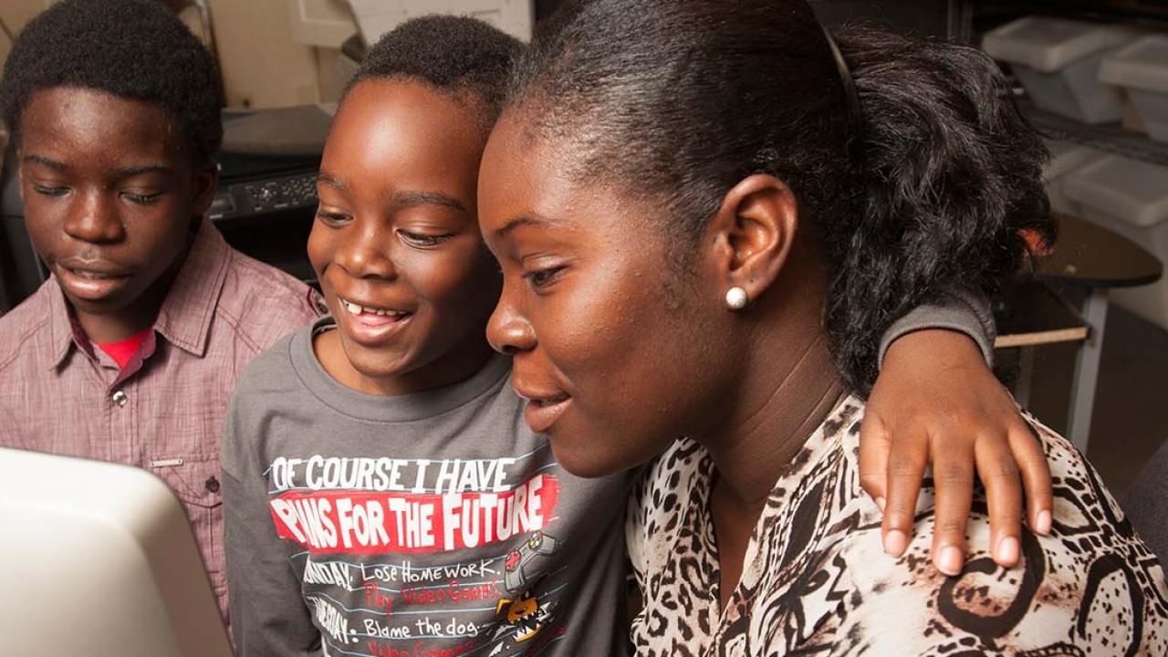 Mother at a computer with two boys next to her, the younger has his arm around his mom's shoulders