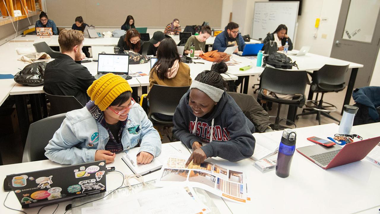 Students works in groups, at tables, in design class.